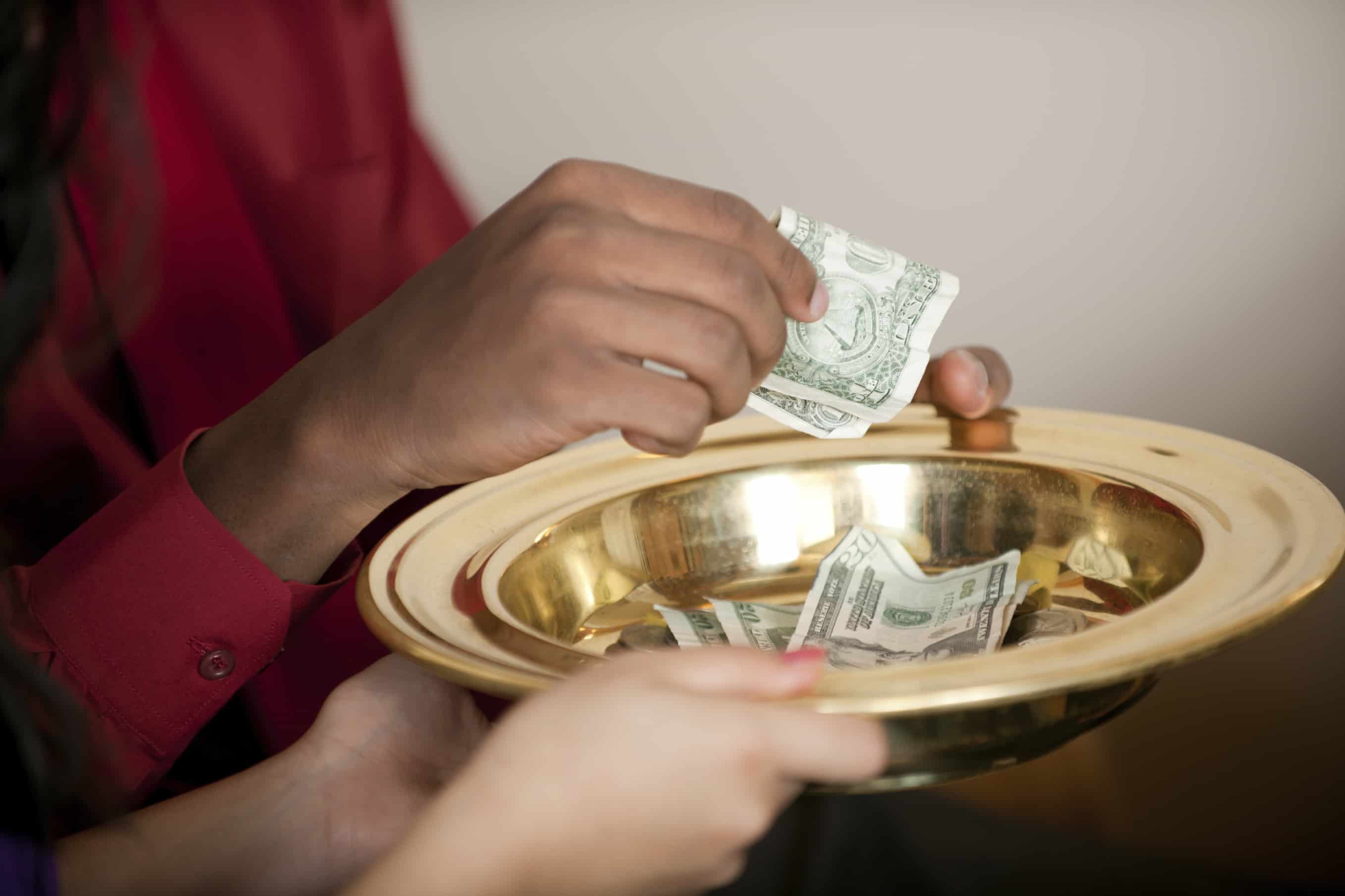 person dropping money in a collection plate